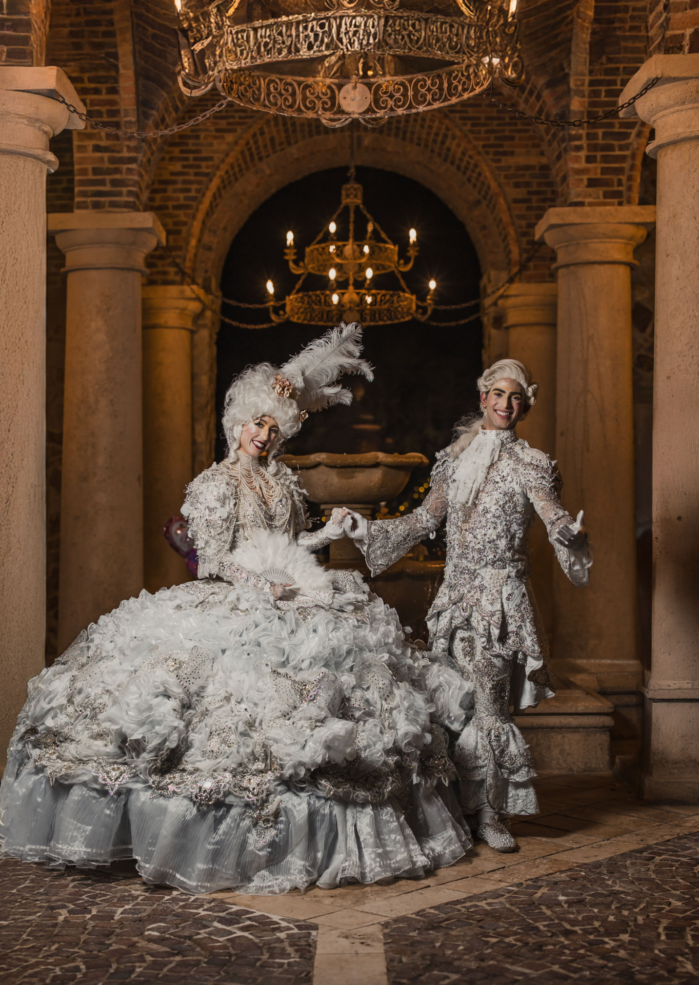 Baroque couple in white period couture beneath a chandelier